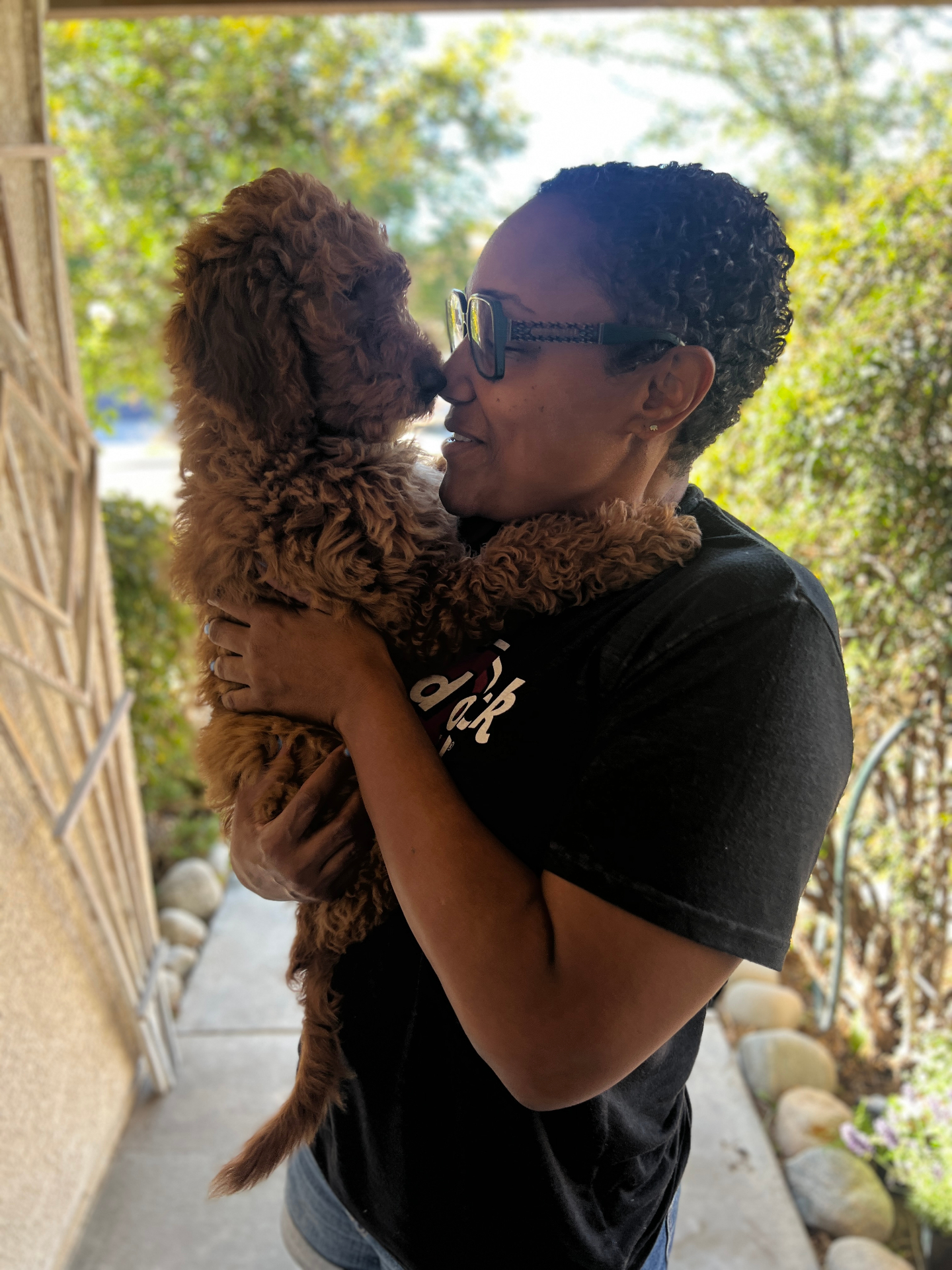 A Kid's Best Doodle owner nose to nose with her red Goldendoodle puppy in a sunlit moment at home